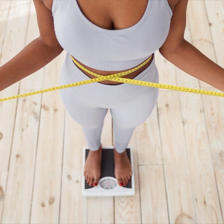 Person standing on a scale measuring waist with a yellow tape